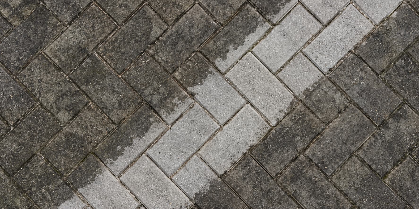 Dirty grey herringbone block paving with a clean, freshly washed stripe running across it